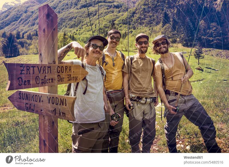 Slovenia, Bovec, four anglers posing at signpost on meadow near Soca river meadows smiling smile man men males standing sign post direction sign guidepost