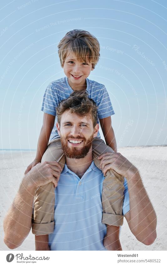 Portrait of father carrying son piggyback on the beach beaches sons manchild manchildren smiling smile pa fathers daddy dads papa happiness happy family