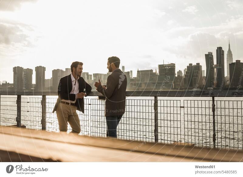 USA, New York City, two businessmen talking at East River New York State Businessman Business man Businessmen Business men speaking males United States