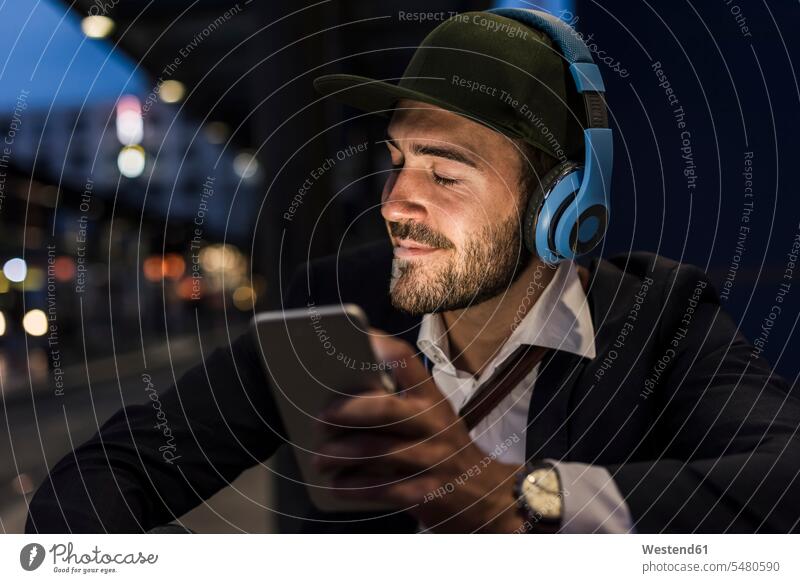 Young man in the city with headphones and cell phone in the evening mobile phone mobiles mobile phones Cellphone cell phones men males headset town cities towns
