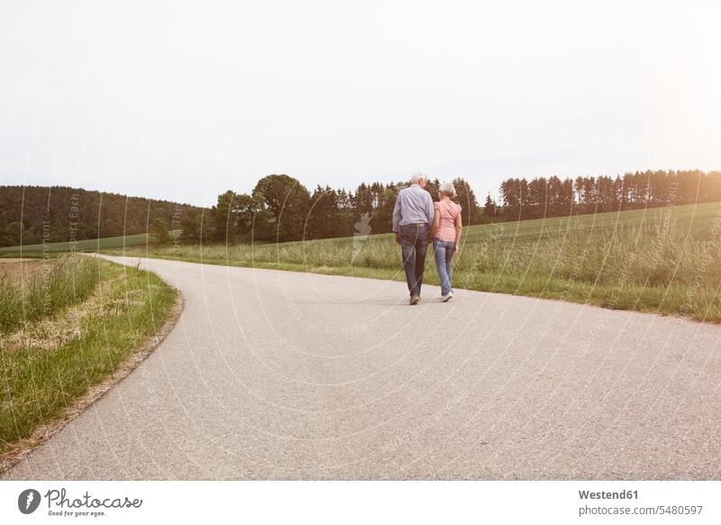 Senior couple walking on country road going twosomes partnership couples rural road rural roads country roads people persons human being humans human beings