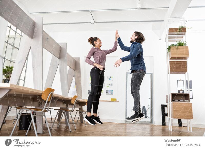 Two happy colleagues in office jumping and high fiving offices office room office rooms workplace work place place of work happiness Leaping High Five Hi-Five