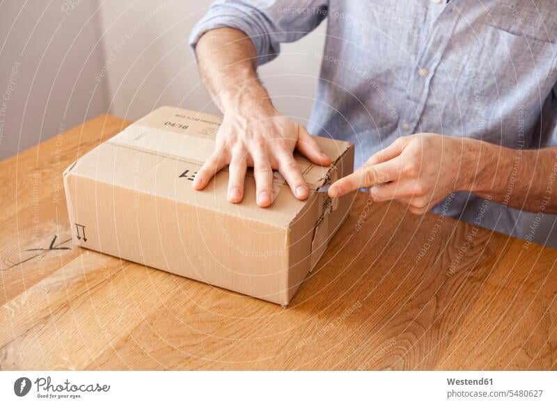 Man's hand unpacking cardboard box with a knife caucasian caucasian ethnicity caucasian appearance european arm arms focus on foreground Focus In The Foreground