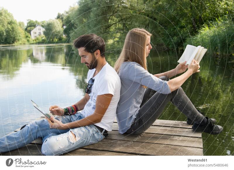 Young couple sitting on jetty at a lake with book and tablet digitizer Tablet Computer Tablet PC Tablet Computers iPad Digital Tablet digital tablets reading