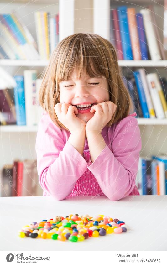 Portrait of smiling little girl with closed eyes with jelly beans lying on a table bookshelf book shelf bookshelves Book Shelves anticipation hopeful childhood