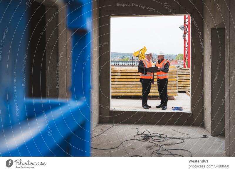 Two men wearing safety vests talking in building under construction working At Work speaking man males construction site Building Site sites Building Sites