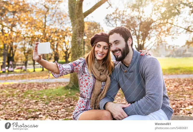 Happy couple taking selfie with smartphone in autumnal park fall twosomes partnership couples Selfie Selfies people persons human being humans human beings