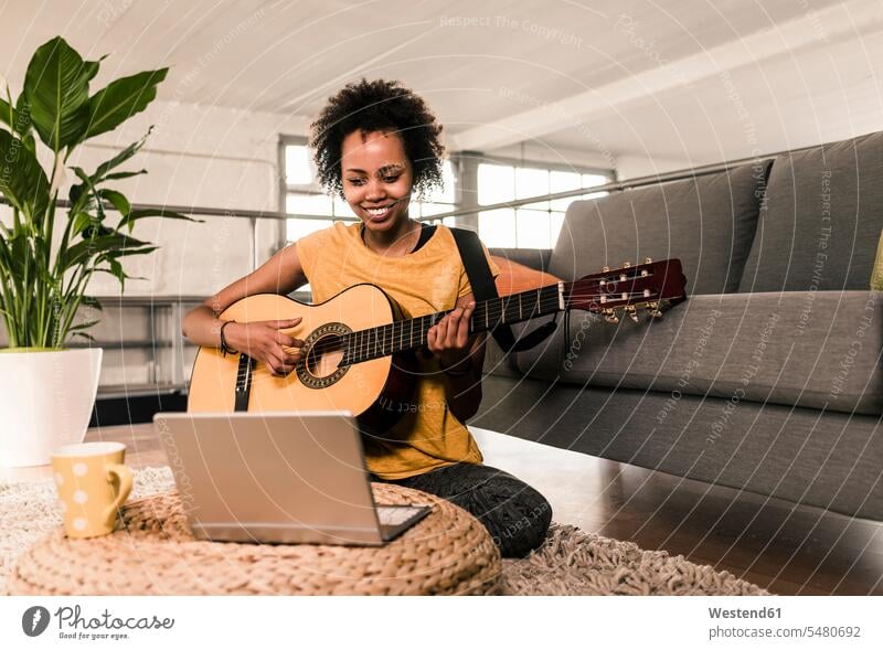 Smiling young woman at home playing guitar looking at laptop Laptop Computers laptops notebook smiling smile females women guitars computer computers Adults