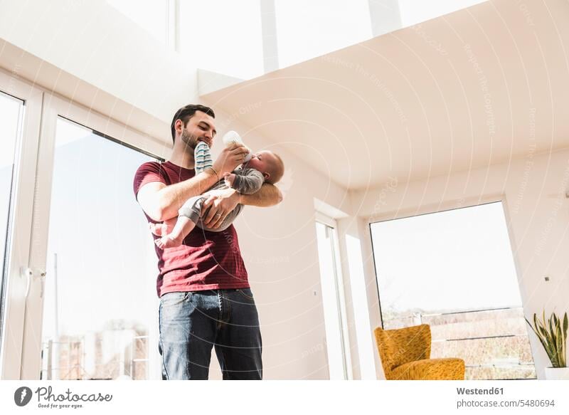 Father bottle feeding his baby son home at home bottle-feeding father pa fathers daddy dads papa flask Flasks babies infants parents family families people
