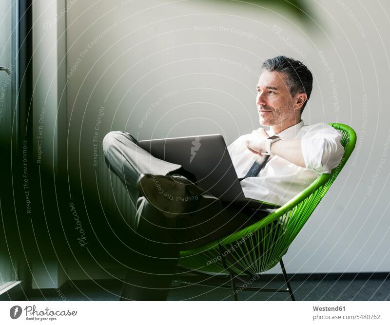 Smiling businessman with laptop sitting in an armchair Laptop Computers laptops notebook Businessman Business man Businessmen Business men computer computers