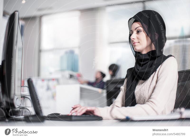 Young woman wearing hijab working on desk in office females women offices office room office rooms portrait portraits headscarf head scarf head scarves