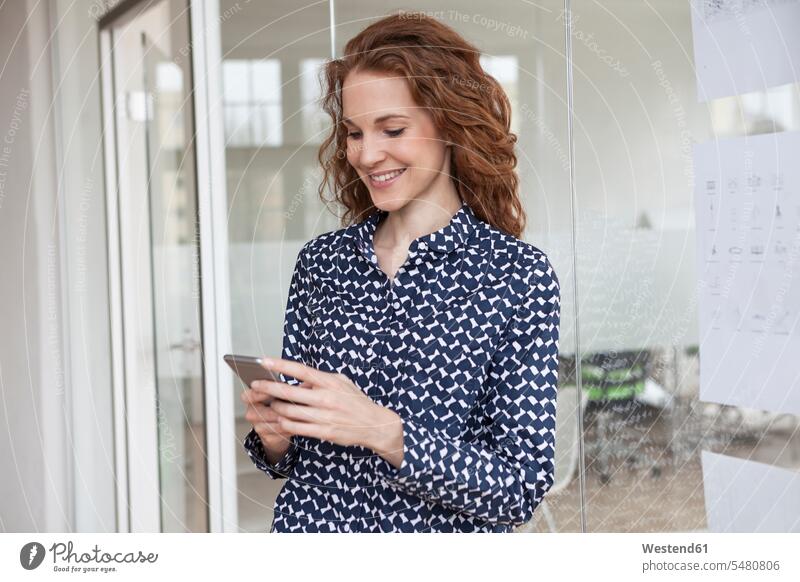 Smiling woman in office looking at cell phone females women smiling smile offices office room office rooms mobile phone mobiles mobile phones Cellphone