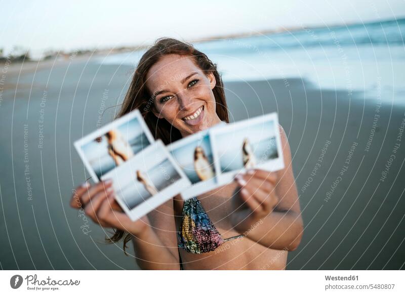 Young woman showing instant photos on the beach photograph photographs smiling smile females women beaches image images picture pictures Adults grown-ups
