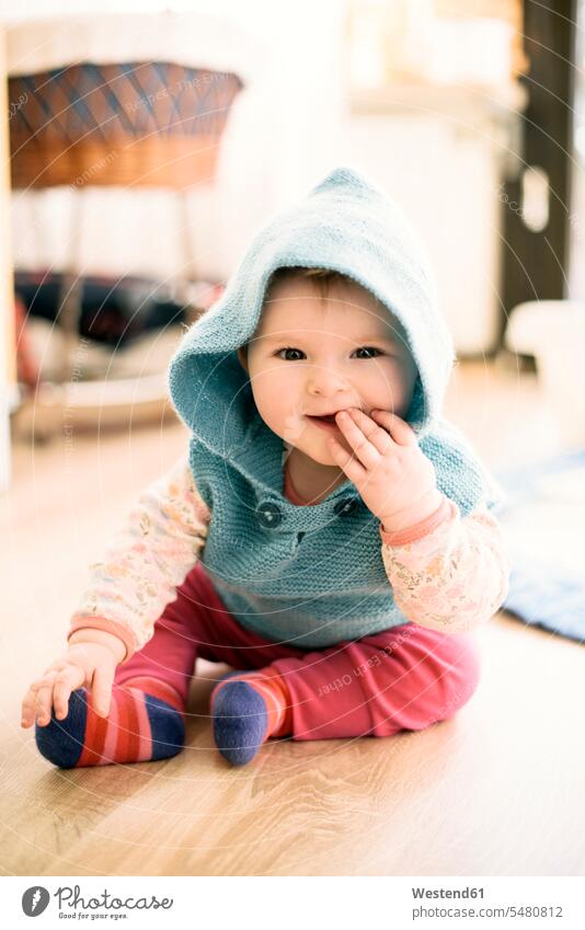 Portrait of smiling baby girl wearing hooded jacket sitting on the floor with finger in mouth caucasian caucasian ethnicity caucasian appearance european