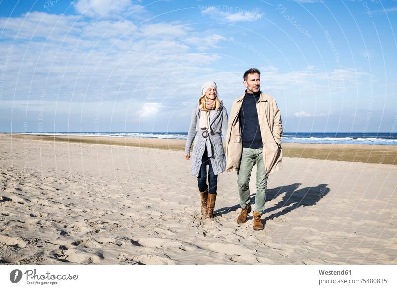 Couple in warm clothing walking on the beach beaches smiling smile couple twosomes partnership couples people persons human being humans human beings vacation