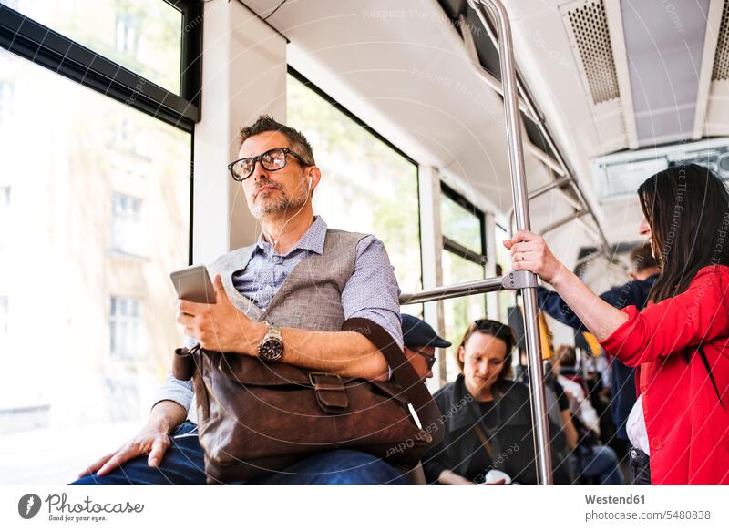 Businessman with smartphone and earphones travelling in tram men males tramway tramways streetcars trams mobile phone mobiles mobile phones Cellphone cell phone