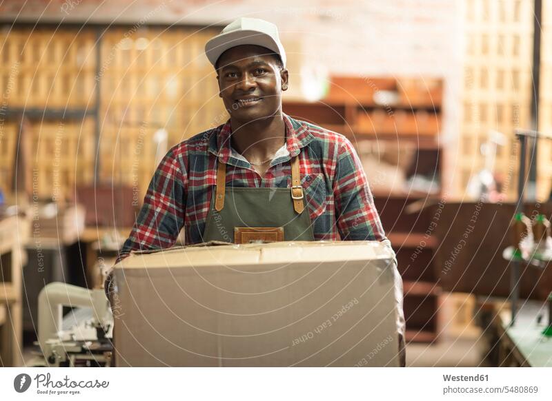 Portrait of smiling man carrying cardboard box in workshop men males smile working At Work Cardboard Carton carton cardboard boxes Cardboards cartons Adults