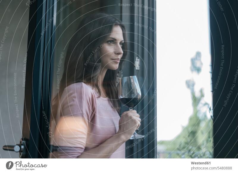 Smiling woman holding glass of red wine looking out of window Red Wine Red Wines relaxed relaxation smiling smile females women windows Alcohol