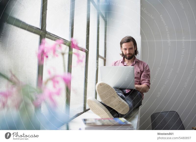 Man sitting on window sill using laptop Laptop Computers laptops notebook Seated man men males windowsill sills window sills Window Cill windowsills home
