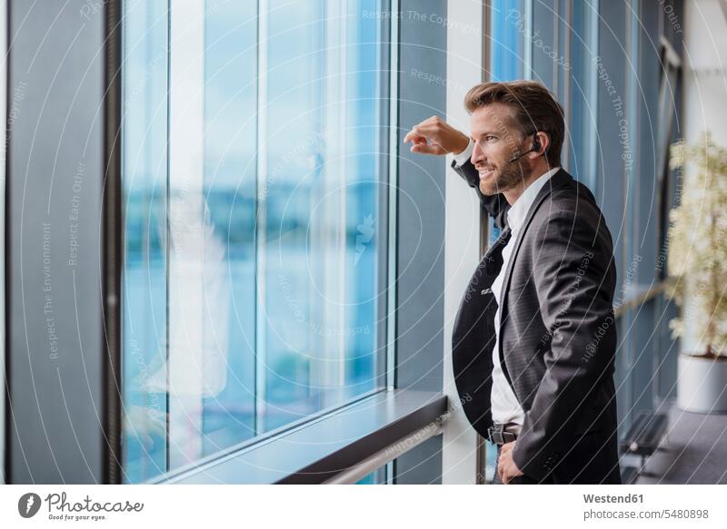Relaxed businessman with bluetooth headset standing in his office looking out of the window headsets on the phone call telephoning On The Telephone calling