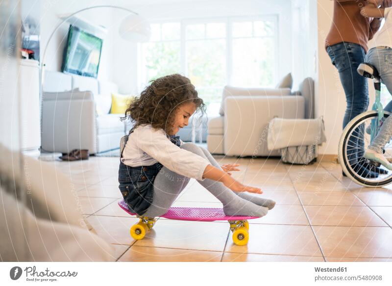 Little girl sitting on skateboard, having fun living room living rooms livingroom Seated playing learning balancing balance Skate Board skateboards practicing