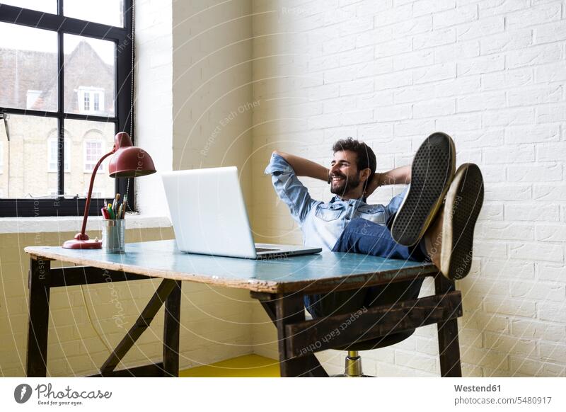 Smiling man sitting with feet up at desk looking out of window men males break Adults grown-ups grownups adult people persons human being humans human beings