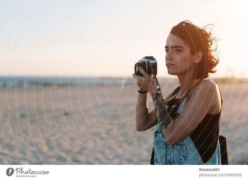 USA, New York, Coney Island, young woman taking photos on the beach at sunset camera cameras searching seek seeking waist up Waist-Up upper body upper part shot
