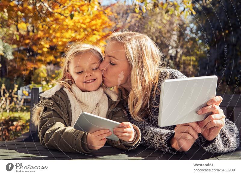 Mother with daughter at garden table holding tablet and cell phone daughters mother mommy mothers ma mummy mama happiness happy smiling smile mobile phone