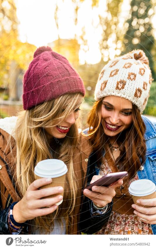 Two young women with smartphone in a park in autumn parks mobile phone mobiles mobile phones Cellphone cell phone cell phones smiling smile female friends