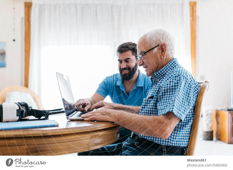 Adult grandson teaching his grandfather to use laptop grandpas granddads grandfathers senior men senior man elder man elder men senior citizen grandsons