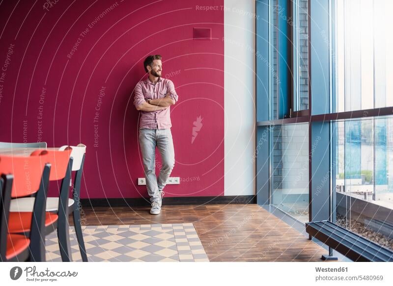 Man leaning against purple wall in modern office looking out of window man men males Adults grown-ups grownups adult people persons human being humans