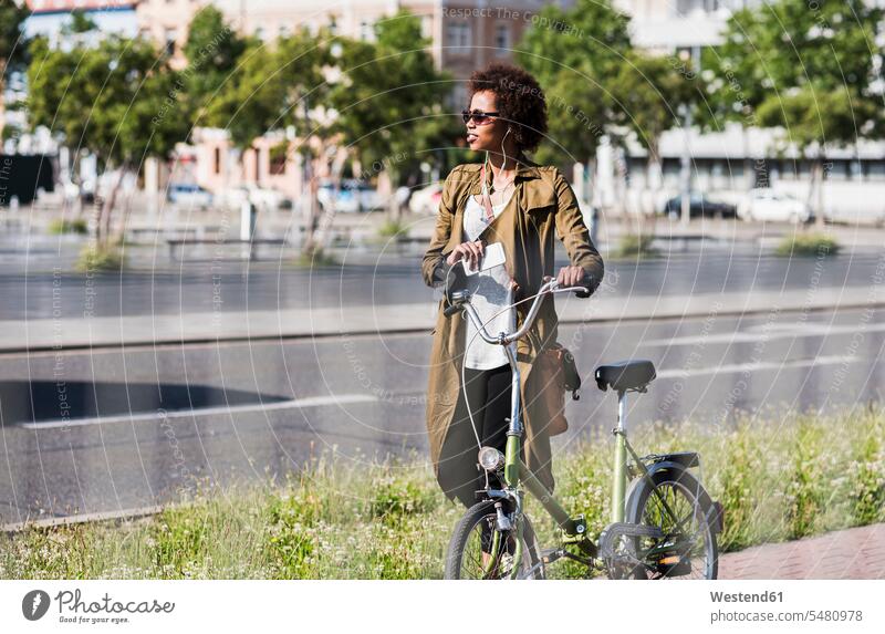 Young woman with smartphone and earphones pushing bicycle females women bikes bicycles Adults grown-ups grownups adult people persons human being humans