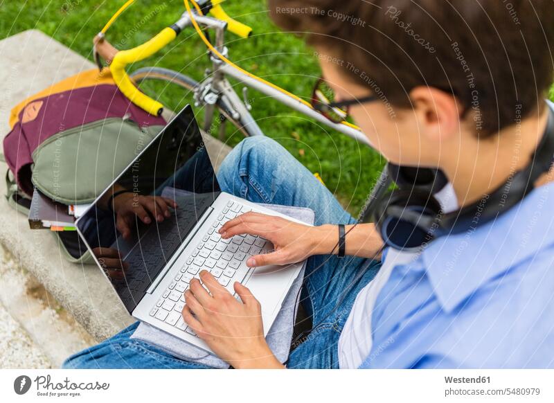 Young man with racing cycle sitting on a bench using laptop, elavated view men males Laptop Computers laptops notebook Adults grown-ups grownups adult people