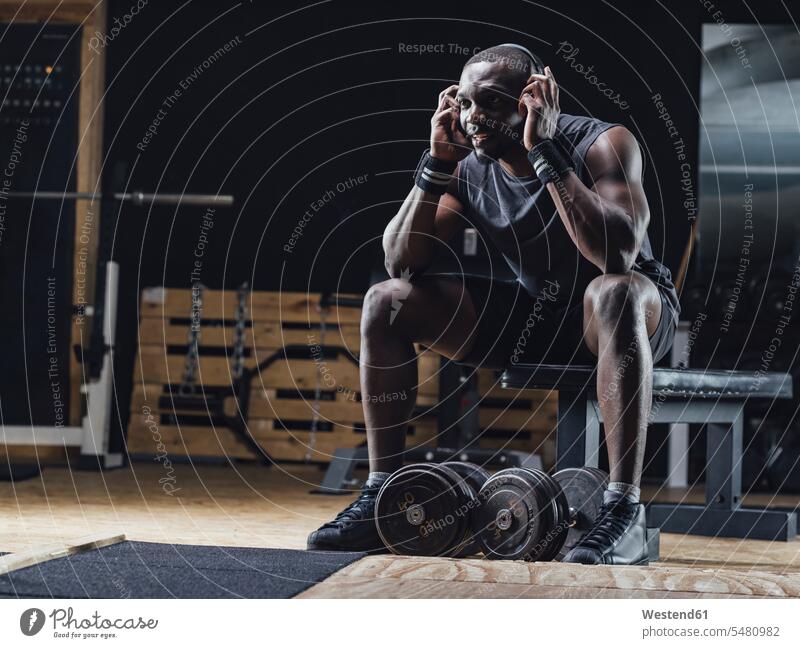 Athlete sitting in gym, wearing headphones, concentrating weight weights Muscular Build muscular muscles athletic gyms Health Club athlete Sportspeople