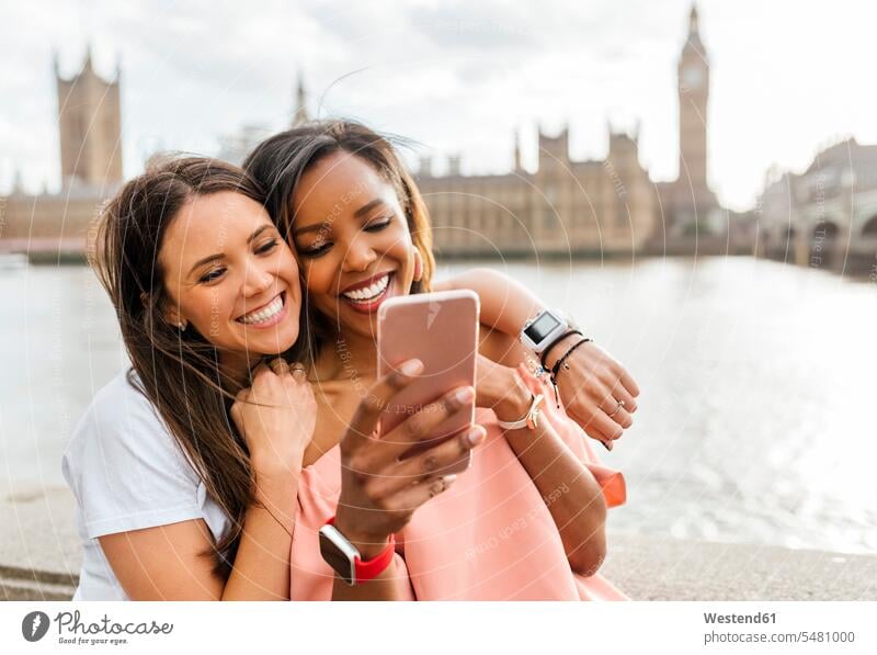 UK, London, two happy women with smartphone near Westminster Bridge woman females Selfie Selfies female friends smiling smile mobile phone mobiles mobile phones
