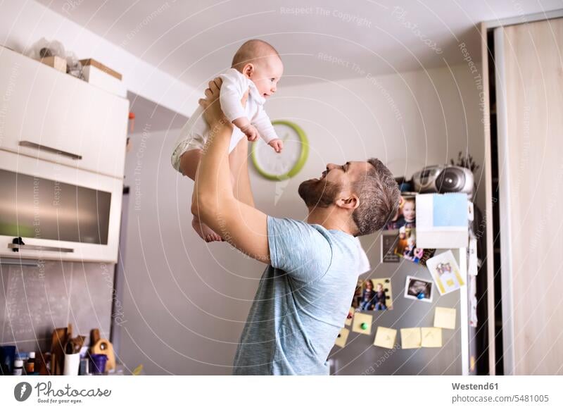 Father holding baby son in kitchen father pa fathers daddy dads papa domestic kitchen kitchens carrying infants nurselings babies parents family families people