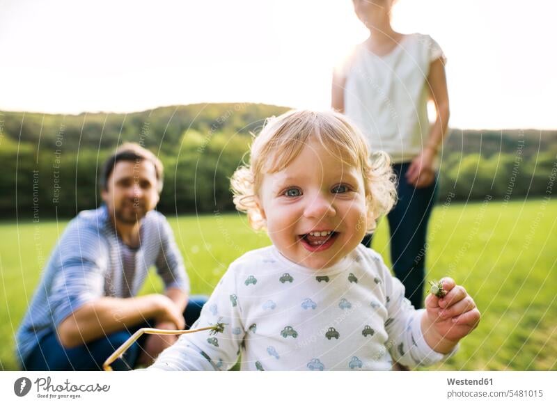 Cute little boy on meadow with parents in background baby infants nurselings babies Fun having fun funny laughing Laughter portrait portraits people persons
