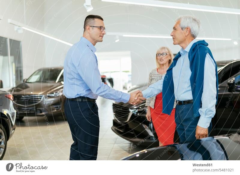 Senior couple couple talking with salesperson in car dealership twosomes partnership couples seller sellers advising counseling advise choosing select choose