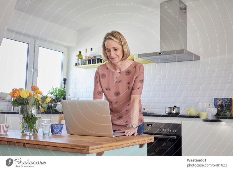Mature woman at home using laptop in kitchen Laptop Computers laptops notebook females women computer computers Adults grown-ups grownups adult people persons