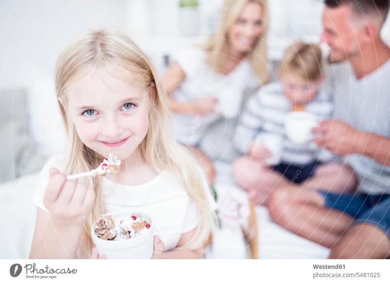 Portrait of smiling girl eating from cereal bowl with family in background portrait portraits females girls smile child children kid kids people persons