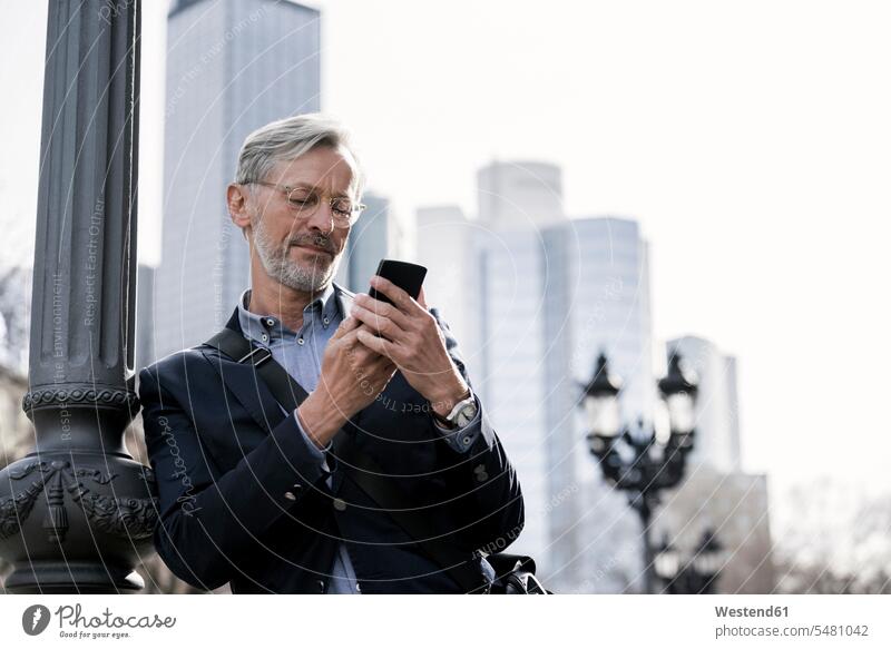 Grey-haired businessman looking at smartphone standing next to street lamp Businessman Business man Businessmen Business men mobile phone mobiles mobile phones