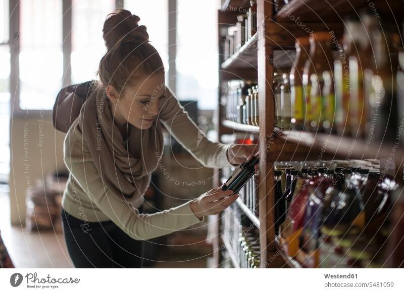 Woman looking at bottle in shelf in shop taking take Bottle Bottles Shelve rack racks shelves shopping woman females women retail trade trading buying Adults