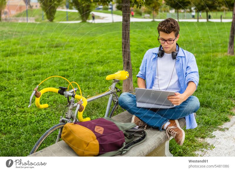 Young man with racing cycle sitting on a bench using laptop Laptop Computers laptops notebook men males computer computers Adults grown-ups grownups adult