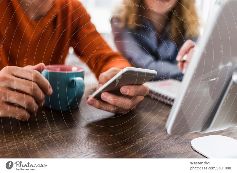 Two colleagues at desk with cell phone and digital tablet mobile phone mobiles mobile phones Cellphone cell phones telephones communication telecommunication