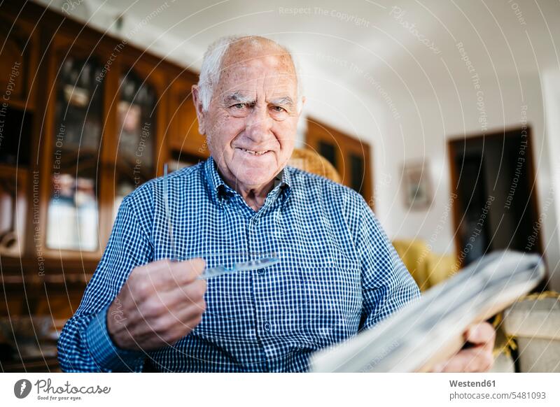 Portrait of smiling senior man with newspaper at home caucasian caucasian ethnicity caucasian appearance european confidence confident low angle view