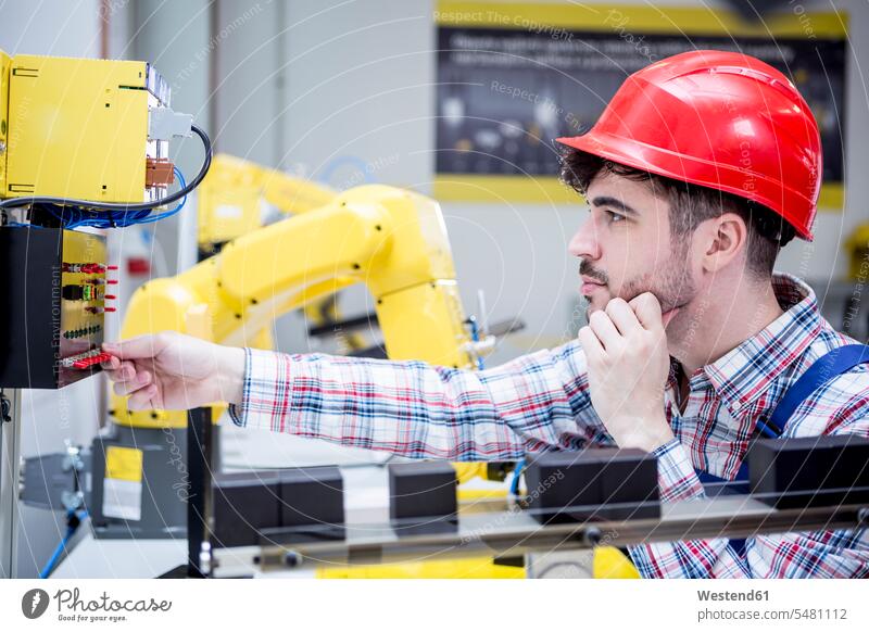 Man wearing hard hat adjusting industrial robot working At Work switch on switching on factory factories Robot industry technology technologies Technological