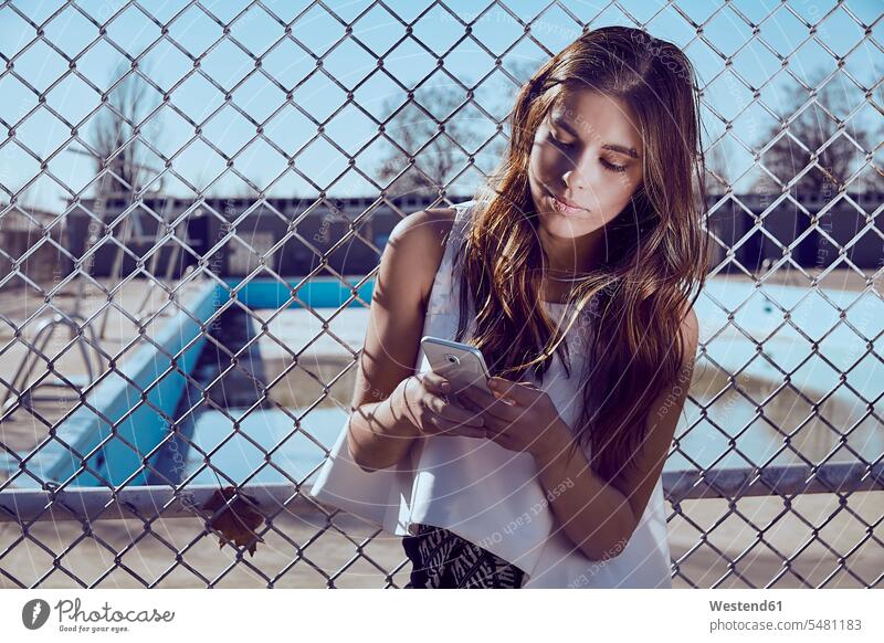Attractive young woman at a fence looking on cell phone mobile phone mobiles mobile phones Cellphone cell phones females women telephones communication