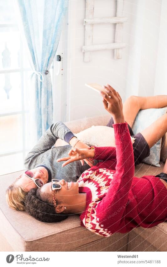 Young couple wearing sunglasses taking selfie on the couch Selfie Selfies twosomes partnership couples lying laying down lie lying down people persons