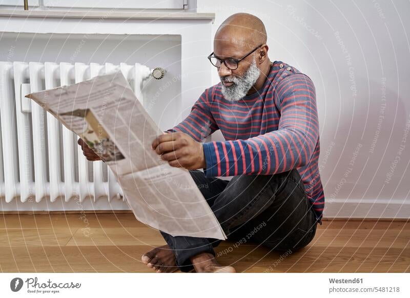 Mature man sitting on thefloor, reading newspaper barefoot naked feet naked foot Barefeet Bare Feet Bare Foot Barefooted bare-footed men males home at home