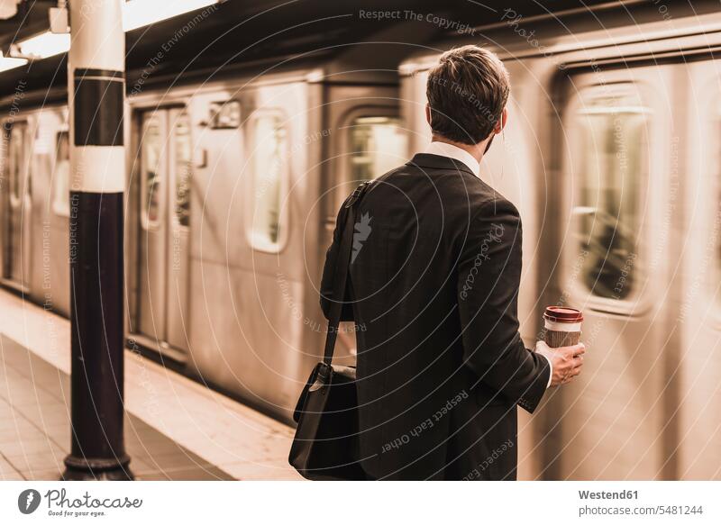 Young businessman waiting at metro station platform, holding disposable cup Businessman Business man Businessmen Business men Railroad Platform Coffee Mug